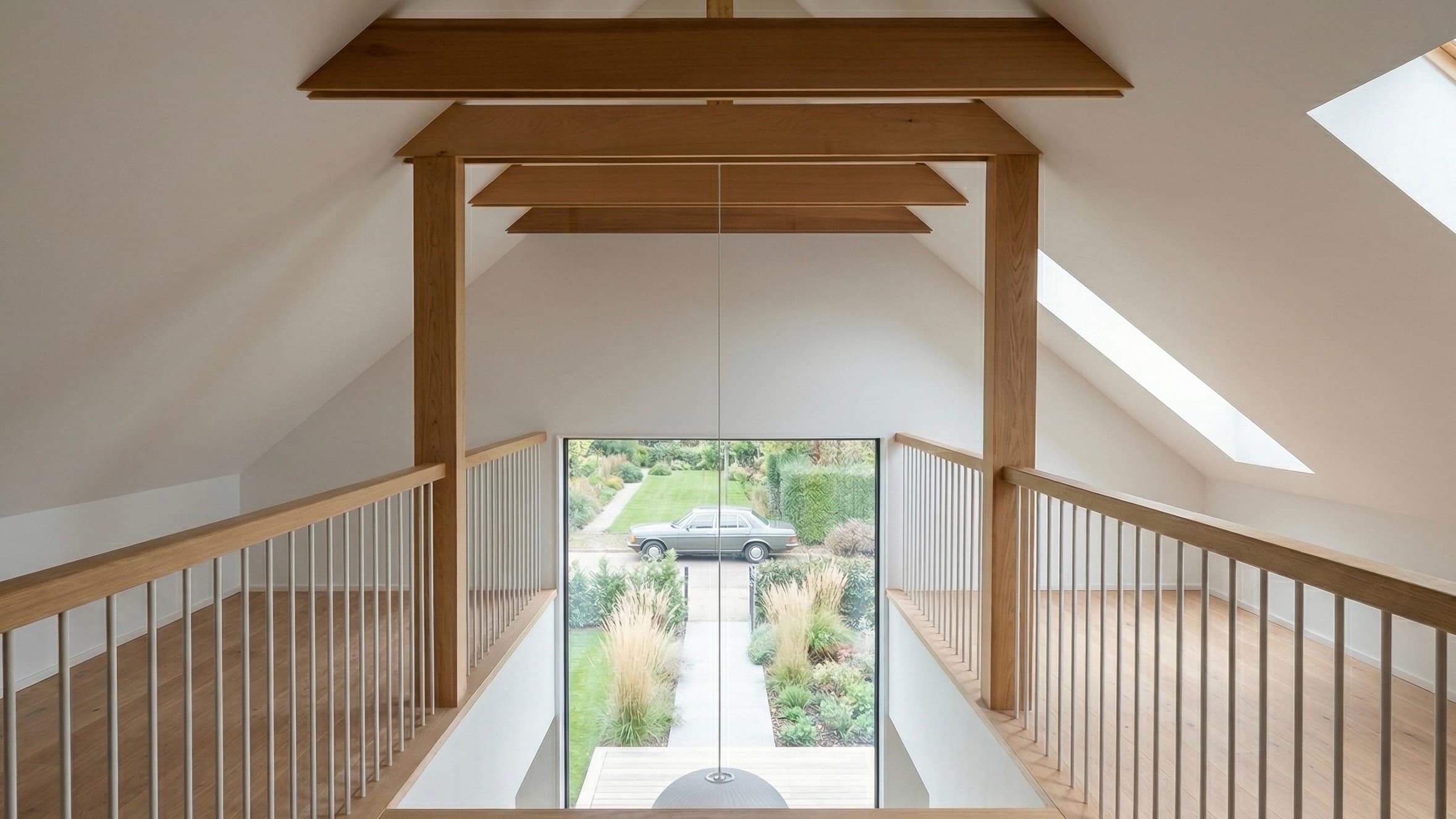 Open loft with timber beams, skylights and a glass-panel railing
